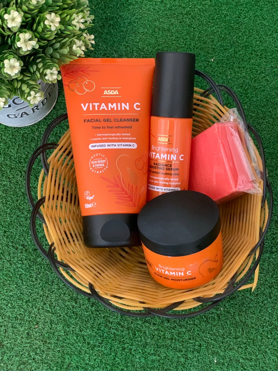 Basket of vitamin C skincare products on green grass with small plant decor.